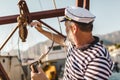Man on pier dressed in a sailor`s shirt and hat holding a sailor rope