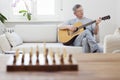 Mature man playing guitar on a couch in a bright living room Royalty Free Stock Photo