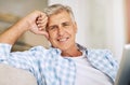 Mature man relaxing, smiling and sitting on his sofa at home on vacation. Older guy comfortable on couch, cheerful and Royalty Free Stock Photo