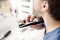 Mature man is shaving off his beard with electric razor at home during quarantine. Handsome bearded man trimming his beard with Royalty Free Stock Photo