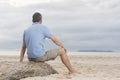 Mature man sitting on a beach looking at the sea with an island Royalty Free Stock Photo