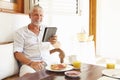 Mature Man Sitting At Breakfast Table Using Digital Tablet Royalty Free Stock Photo