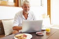 Mature Man Sitting At Breakfast Table Using Laptop Royalty Free Stock Photo