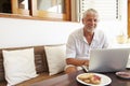 Mature Man Sitting At Breakfast Table Using Laptop Royalty Free Stock Photo