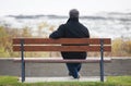 Mature man sitting on park bench overlooking River in Autumn.