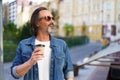 Mature man smiling looking away sideways catching last rays of sun wearing sunglasses with with coffee in paper cup at Royalty Free Stock Photo