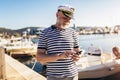 Man standing near the sea dressed in a sailor`s shirt and hat using smart phone