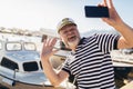 Man standing near the sea dressed in a sailor`s shirt and hat using smart phone