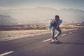Mature man in sunglasses with hands back riding his longboard on country road with mountains in background. Man skating or Royalty Free Stock Photo
