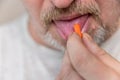 A mature man takes medication. The lower part of the male face. Man puts an orange pill on his tongue with his hand. Male with Royalty Free Stock Photo