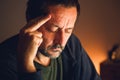 Mature man touching forehead with finger in thoughtful pose, low key warm light emphasizing rethinking and focus Royalty Free Stock Photo