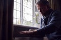 Mature Man Trying To Keep Warm By Radiator At Home During Cost Of Living Energy Crisis