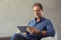 mature man using digital tablet and looking at camera while sitting Royalty Free Stock Photo