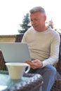 Mature man using laptop while sitting on wicker chair at patio Royalty Free Stock Photo