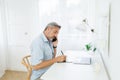 Mature man using mobile phone while writing something on digital tablet Royalty Free Stock Photo