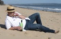 Mature man wearing a hat and sunglasses resting on the beach with a bottle of wine in summer. Royalty Free Stock Photo