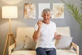 Mature man wearing white T-shirt using his mobile phone for listening to music online through modern headphones at home interior Royalty Free Stock Photo