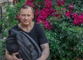 Mature man 60 years old, in a black T-shirt, against a background of bright red flowers with a backpack Royalty Free Stock Photo