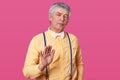 Mature man in yellow shirt, suspenders and white bowtie showing stop sign with hand. Deny to do something, forbids to come closer Royalty Free Stock Photo