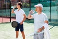 Mature man and young man drink water on padel court