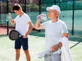 Mature man and young man drink water on padel court