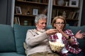 Mature married couple entertaining observing terrified TV program. Senior husband and wife watching horror movie or film at home