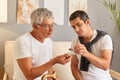 Mature man feeling unwell his adult son giving medicine for sick father putting drops into glasses helping mature male to feel Royalty Free Stock Photo