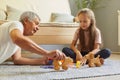 Mature man wearing white t-shirt playing with wooden toys with his granddaughter posing in living room sitting on floor family Royalty Free Stock Photo