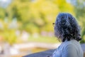 Mature Mexican woman with grayish black hair and glasses, standing pensively on a balcony and reflecting on life