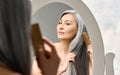 Mature mid aged senior Asian woman looking at mirror combing her gray hair.