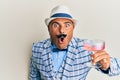 Mature middle east man with mustache wearing vintage and fashion style drinking a cocktail scared and amazed with open mouth for Royalty Free Stock Photo