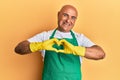 Mature middle east man wearing cleaner apron and gloves smiling in love showing heart symbol and shape with hands