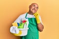 Mature middle east man wearing cleaner apron holding cleaning products serious face thinking about question with hand on chin, Royalty Free Stock Photo