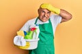 Mature middle east man wearing cleaner apron holding cleaning products stressed and frustrated with hand on head, surprised and Royalty Free Stock Photo