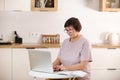 mature old lady working remotely from home office on laptop making notes. Smiling middle aged 50s business woman using Royalty Free Stock Photo