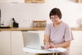 mature old lady working remotely from home office on laptop making notes. Smiling middle aged 50s business woman using Royalty Free Stock Photo