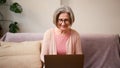 Mature old 60s woman student working at home using laptop technology device sitting on couch at home Royalty Free Stock Photo