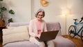 Mature old 60s woman student working at home using laptop technology device sitting on couch at home