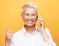 mature old woman with short hair standing isolated over yellow background wall talking by mobile phone. Royalty Free Stock Photo