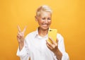 mature old woman with short hair standing isolated over yellow background wall talking by mobile phone. Royalty Free Stock Photo