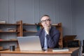 Mature pensive businessman in glasses and suit is thinking about his work by the laptop