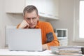 Mature pensive man working remote from home with laptop and files