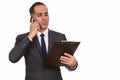 Mature Persian businessman talking on the phone while reading on clipboard Royalty Free Stock Photo