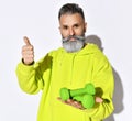 Mature positive hipster brutal bearded man in bright yellow green casual hoodie standing with green dumbbels and showing thumbs up