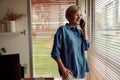 Mature pretty woman at home standing near window while talking by mobile phone Royalty Free Stock Photo