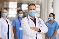 Mature proud doctor with face mask and his medical team in background Royalty Free Stock Photo