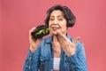 Mature senior woman eating burger with satisfaction. Grandmother enjoys tasty hamburger takeaway, delicious bite of burger, order