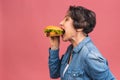 Mature senior woman eating burger with satisfaction. Grandmother enjoys tasty hamburger takeaway, delicious bite of burger, order