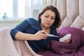 Mature sick upset woman with handkerchief looking at thermometer