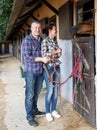 Mature smiling couple with girth feeding a horse at stable Royalty Free Stock Photo